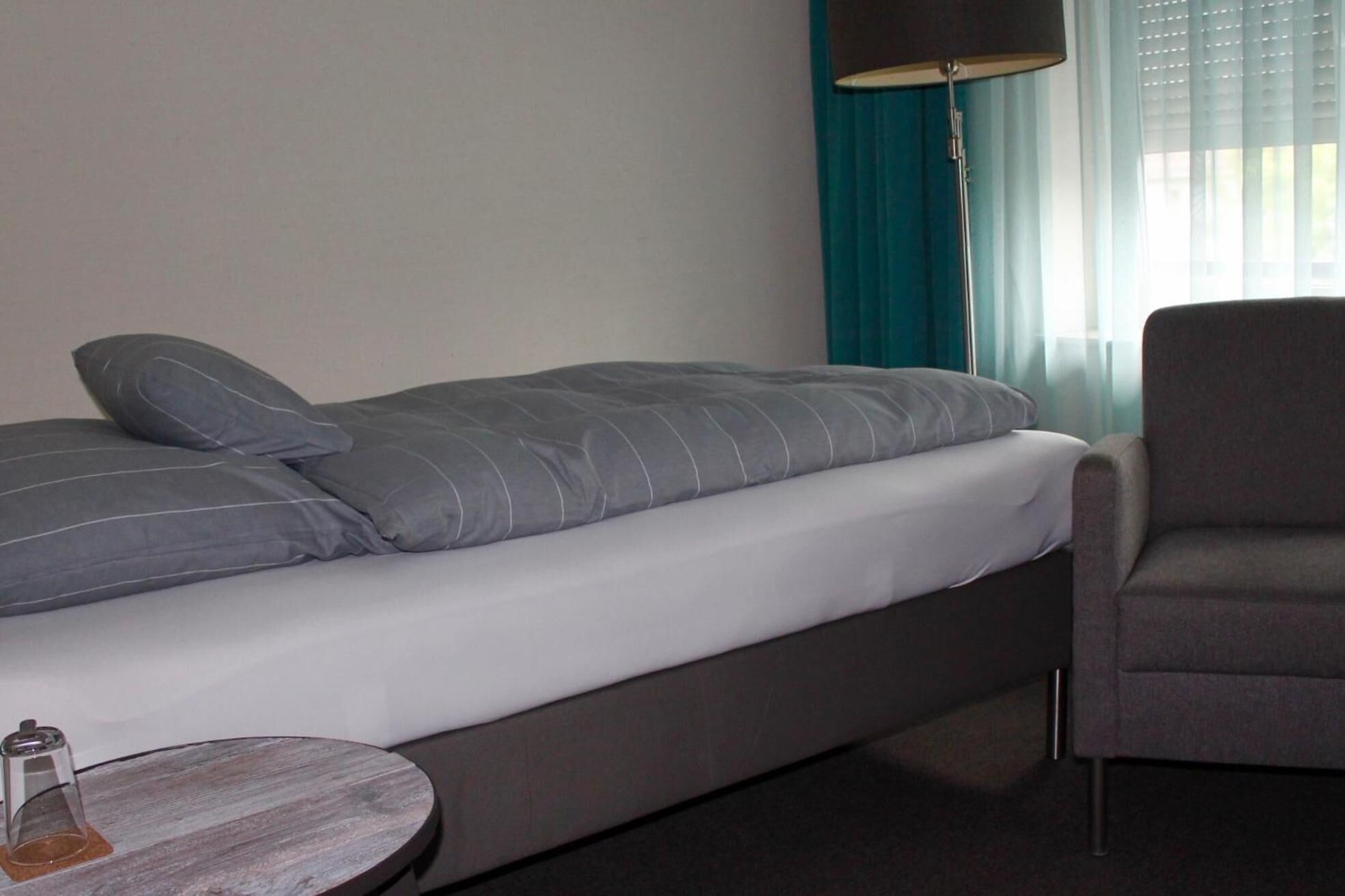 Une chambre d’hôtel moderne avec un lit simple, une petite table ronde, une chaise et une lampe.