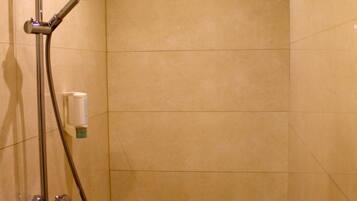 A walk-in shower with a handheld showerhead, a handheld shower nozzle, and a wall-mounted faucet.