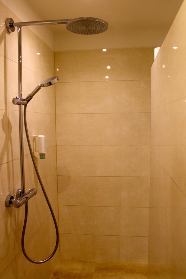 A walk-in shower with a handheld showerhead, a handheld shower nozzle, and a wall-mounted faucet. - Hotel Donnersberg (Darmstadt)