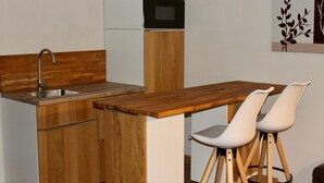 Una kitchenette compacta con horno integrado, un lavamanos y una encimera de madera. Hay dos sillas blancas con patas de madera.