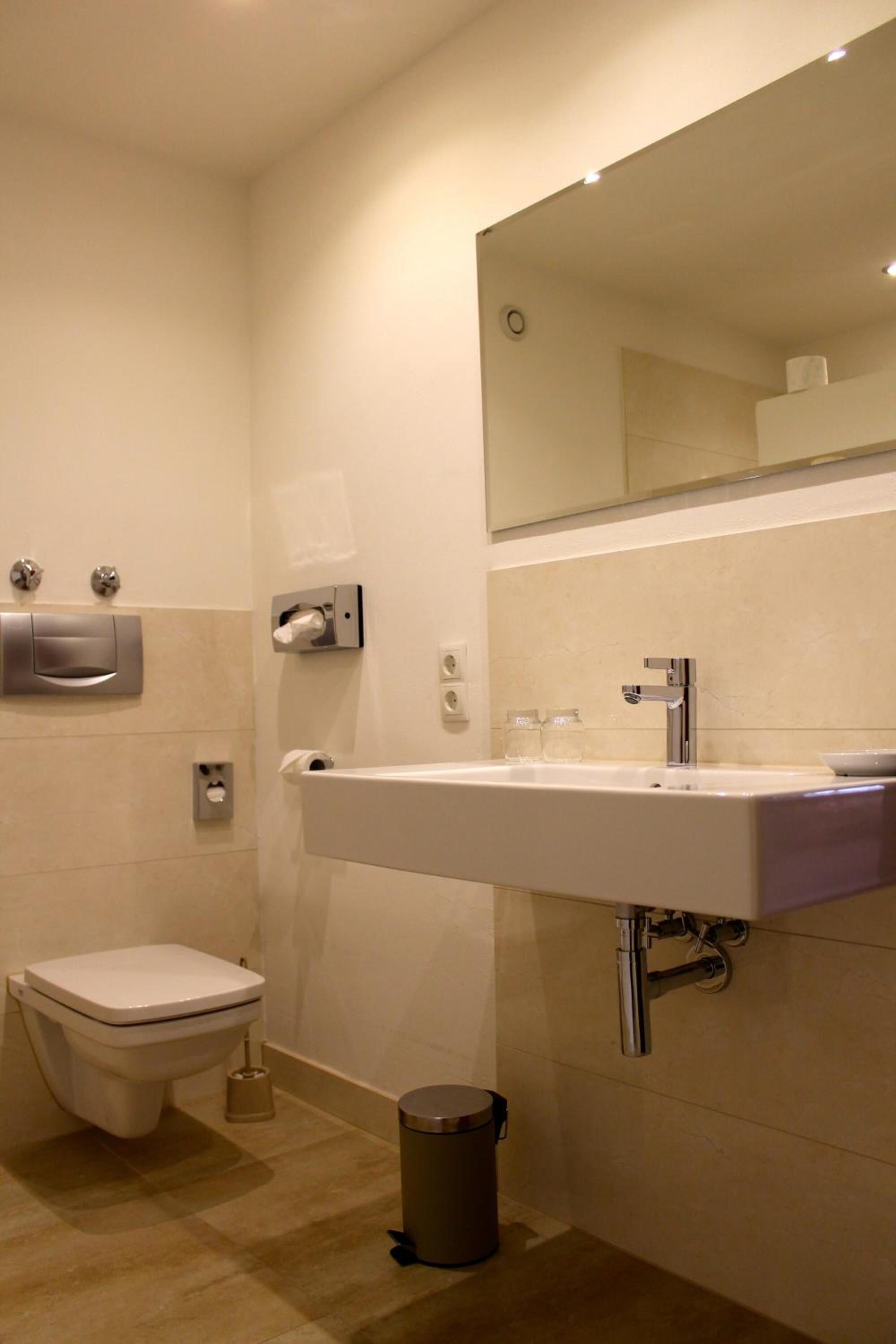 Een moderne badkamer met toilet, wastafel, spiegel en prullenbak.