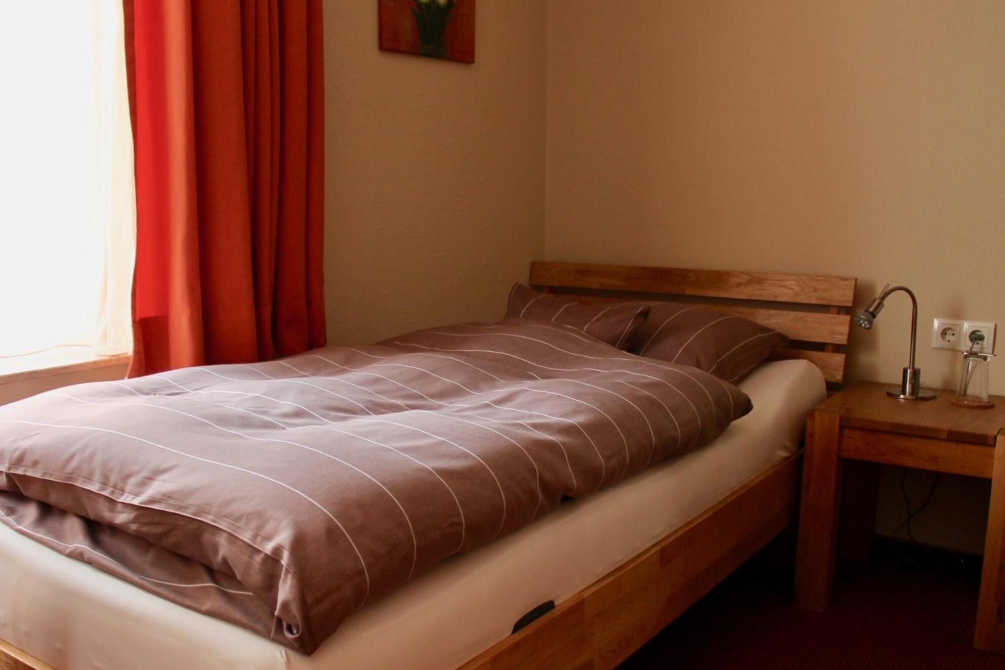 Uma cama de solteiro com cabeceira de madeira, mesa de cabeceira com abajur e tomada.
