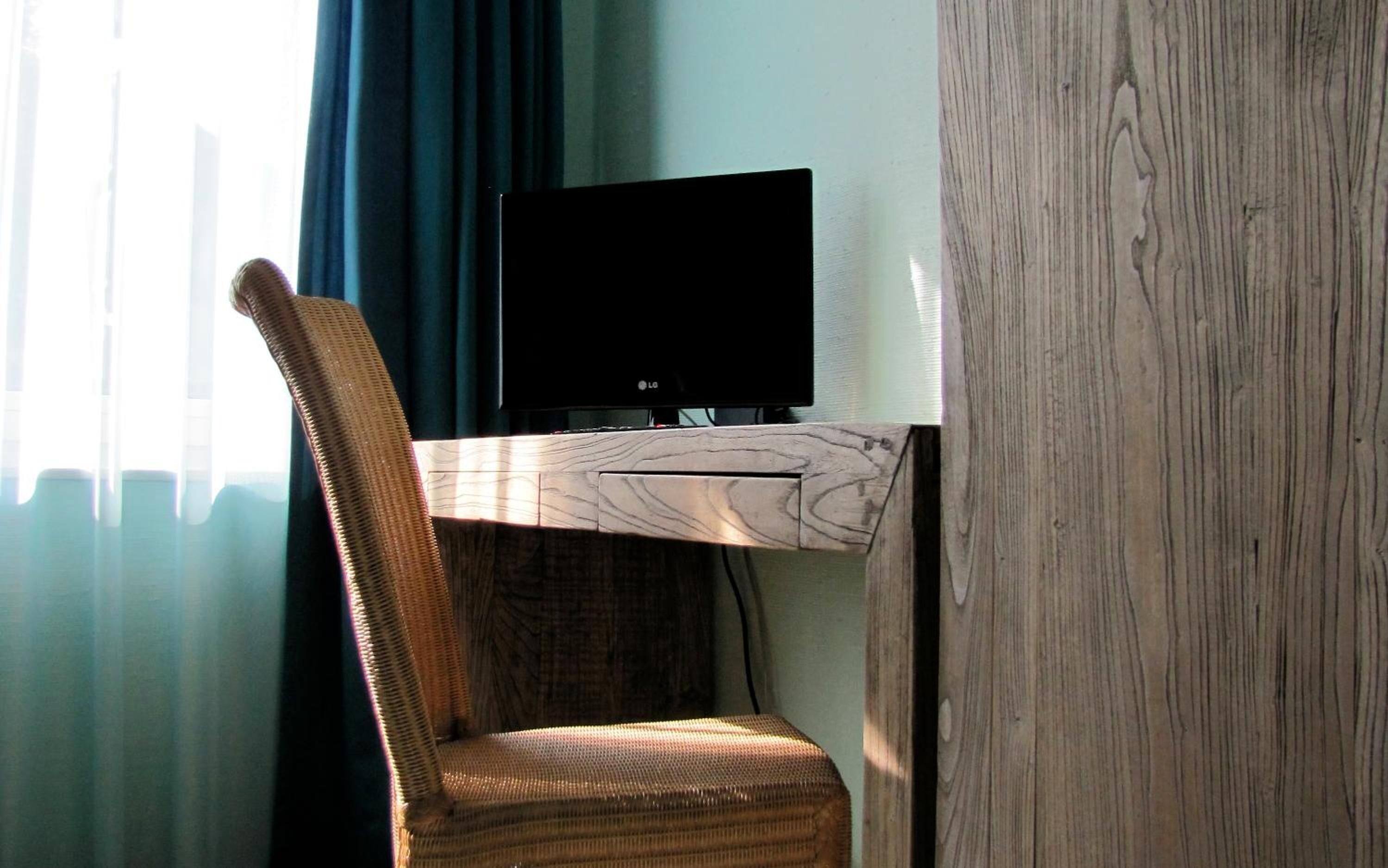 A room with a wooden desk, a television, and a wicker chair.