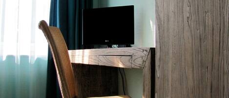 Una habitación con escritorio de madera, televisión y silla de mimbre.