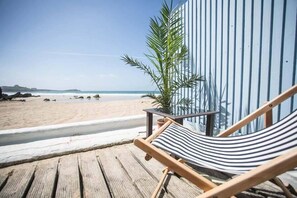 Une terrasse en bois avec un fauteuil-hamac rayé donnant sur une plage.