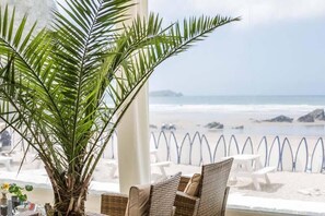 Un espace aménagé avec des sièges situé au bord de la plage, doté de meubles en osier et d’une grande plante en pot.
