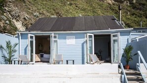 A beach house with an open front door, two chairs outside, and a sign that reads "LUSTY BEACH". - Lusty Glaze Beach Accommodation (Newquay)