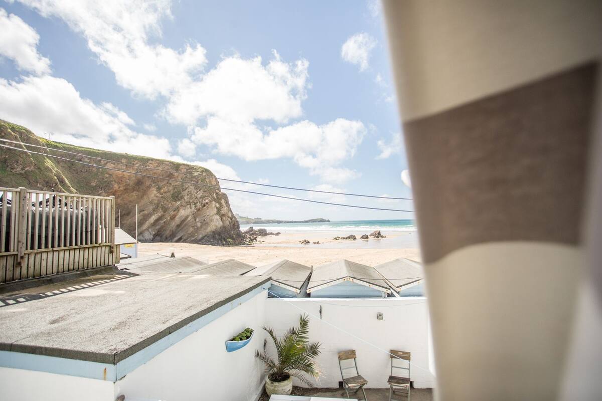 A coastal view with a cliff, beach, and a building with a balcony overlooking the sea.
