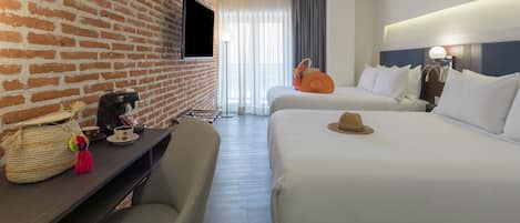 Habitación de hotel con dos camas, una pared de ladrillo, un televisor de pantalla plana, una cafetera, una cesta y un sombrero sobre la cama.
