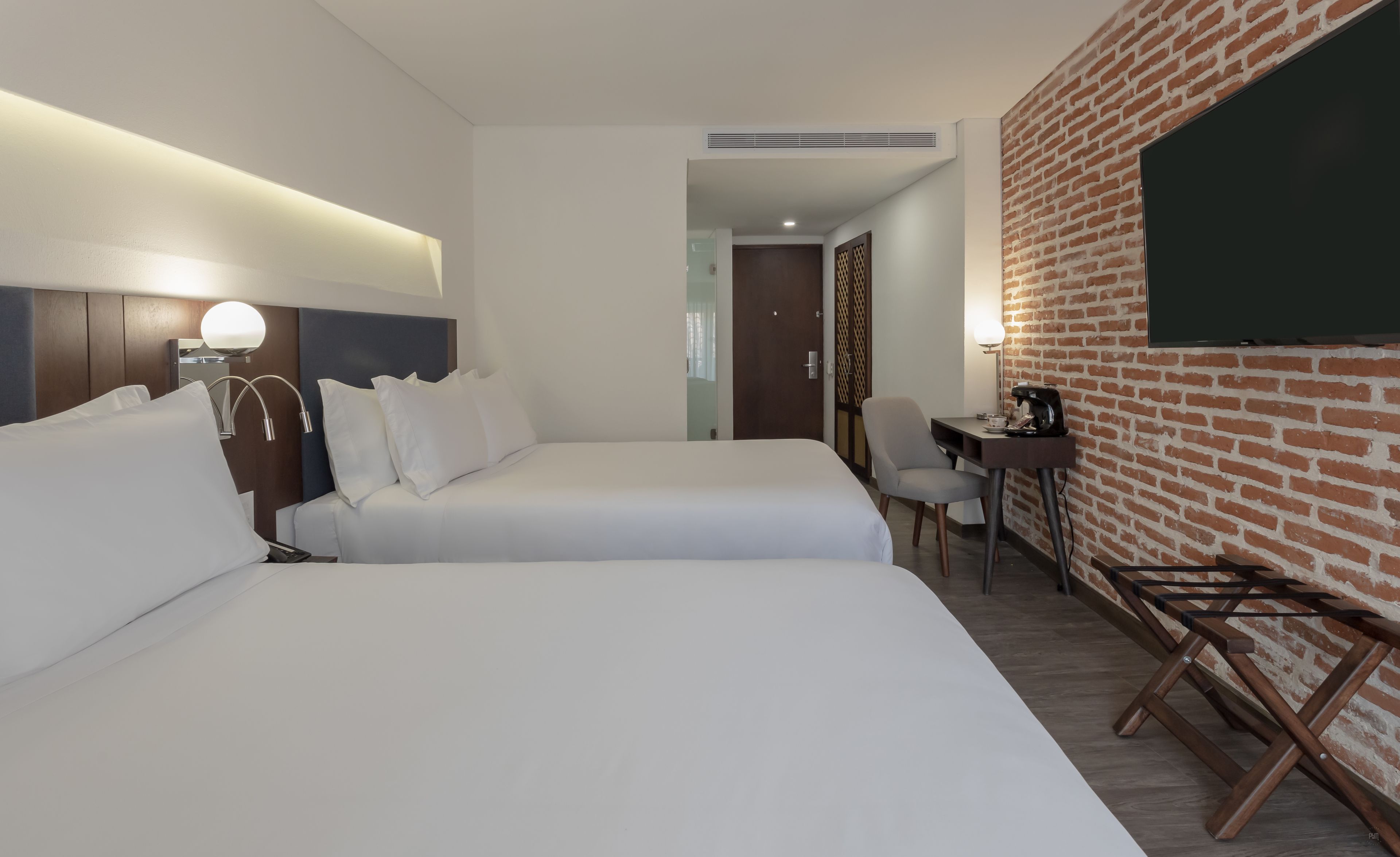 Ein Hotelzimmer mit zwei Betten, einem Schreibtisch mit Stuhl, einer Kaffeemaschine und einer Ziegelwand.