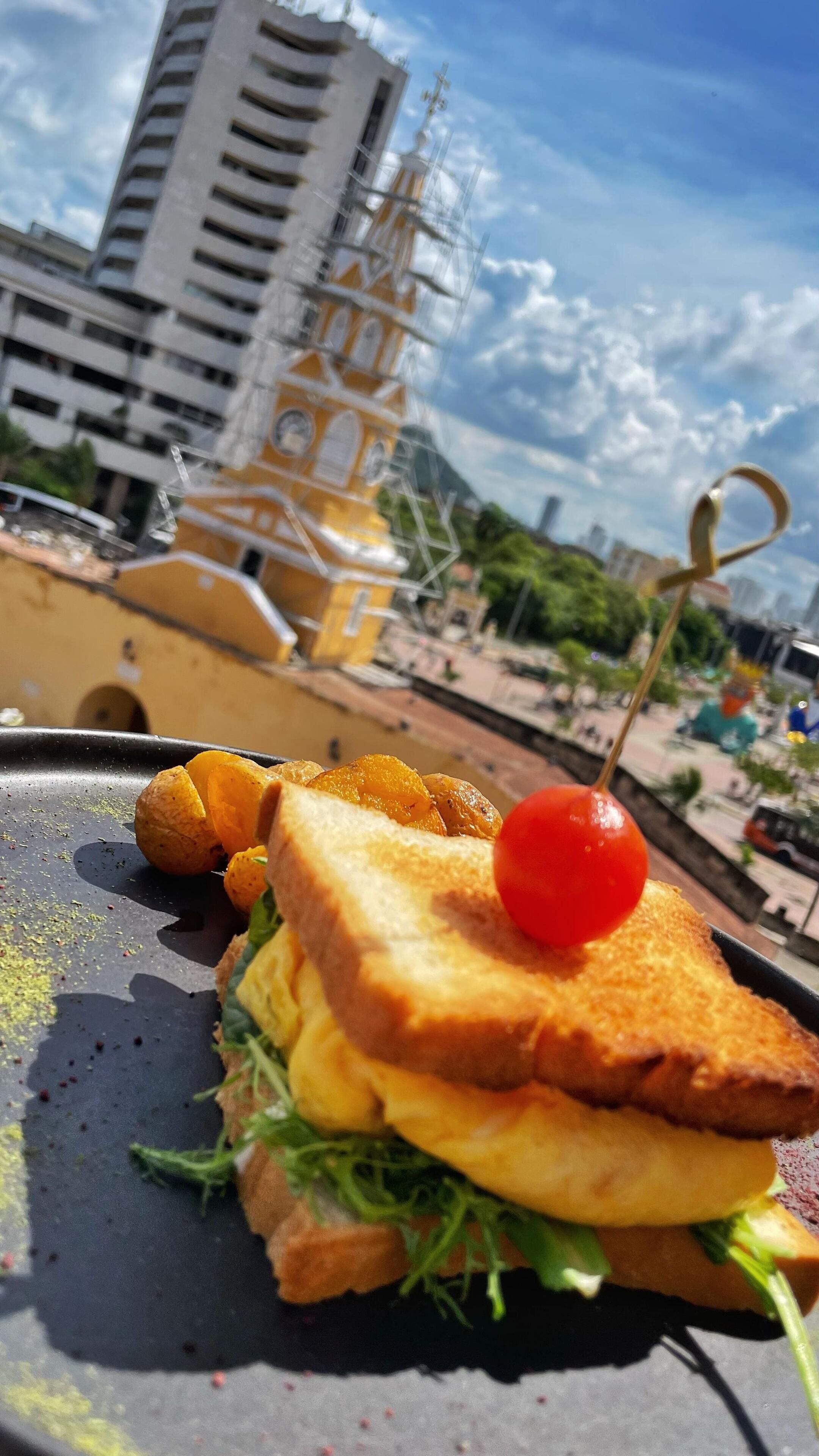 A sandwich with a cherry on top, placed on a black surface with scattered spices.