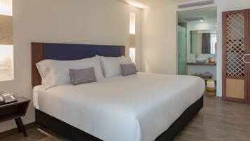 Una cama bien hecha con cabecera de madera, una mesita de noche con teléfono, y un baño visible a través de una puerta abierta.