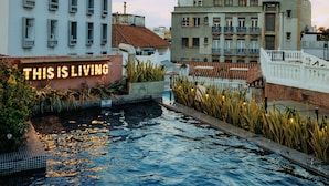 A swimming pool with a sign that reads "THIS IS LIVING" and buildings in the background. - Hotel Santa Catalina By OxoHotel (Cartagena)