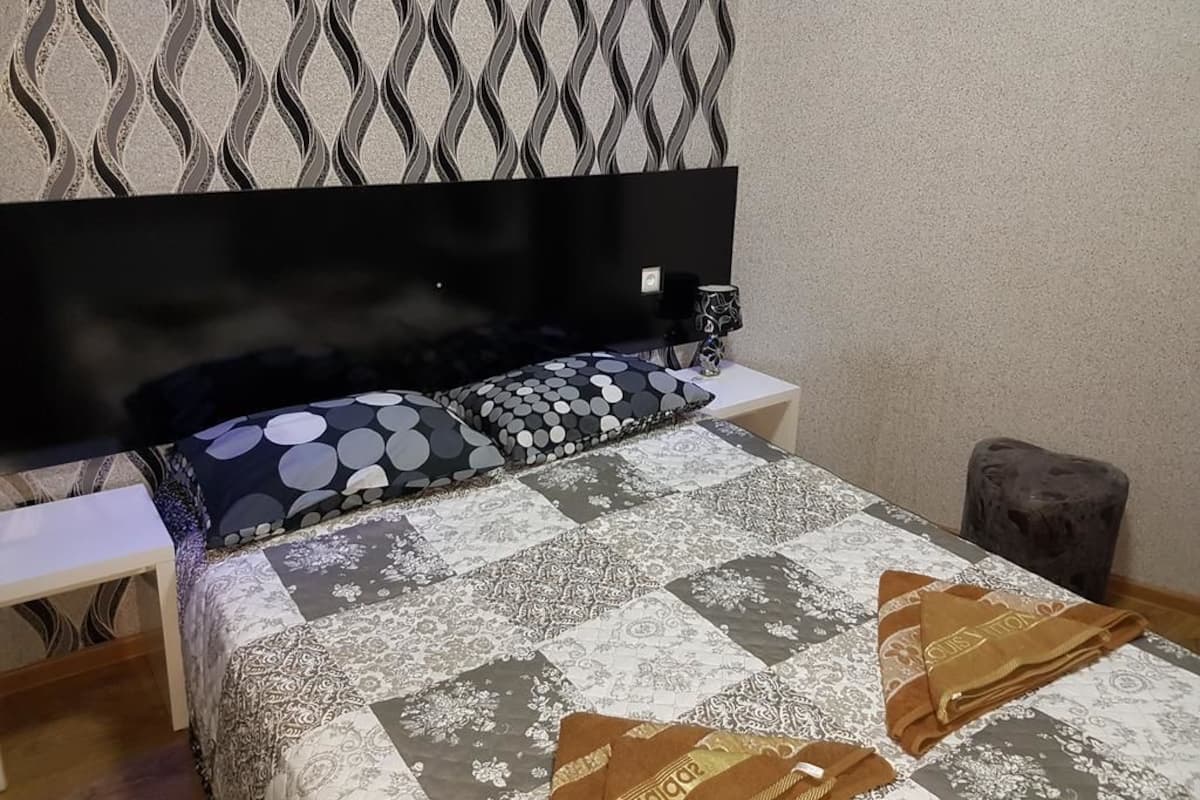 A bedroom with a bed, a nightstand, a TV, and a patterned wall.