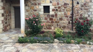 A stone building with a tiled roof, a small window, and a garden with various plants and flowers. - Casa Rural La Dueña (El Pobo de Duenas)
