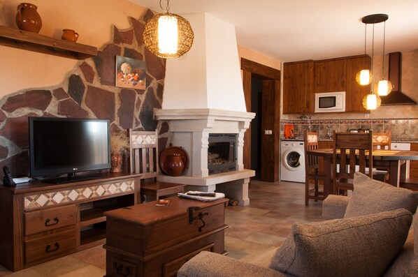 A living room with a TV, fireplace, and stone wall. - Casa Rural La Dueña (El Pobo de Duenas)