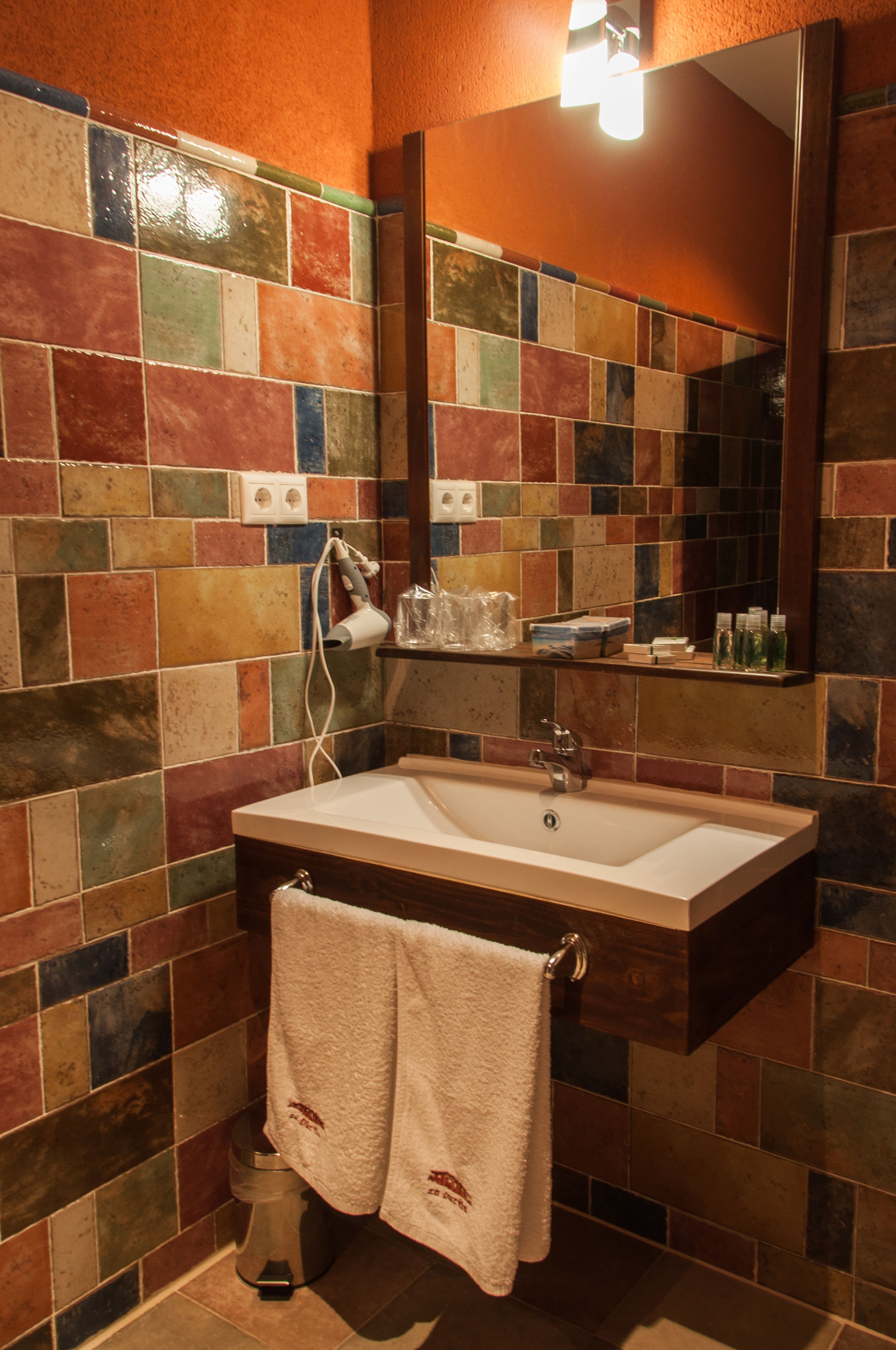A bathroom with a tiled wall, a sink, a mirror, and a towel rack.