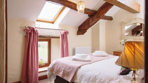 A bedroom with a skylight, a bed with white linens, a bedside lamp, and a window with curtains. - Low Barn Cottage (Brampton)