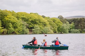 A group of people in a green rowboat on a lake with dense green trees in the background. - Gelt Cottage (Brampton)