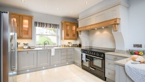 Una cocina moderna con gabinetes grises, un refrigerador de acero inoxidable, un horno empotrado y un ventanal con vistas a áreas verdes.