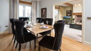 Un comedor con una mesa de madera preparada para cuatro, sillas negras tapizadas con detalles de tachuelas, y una araña colgante.