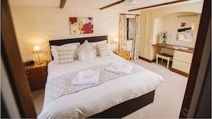Un dormitorio ordenado con una cama, lámparas de noche, mesitas de noche, cómoda, espejo y un cuadro con motivos florales en la pared.