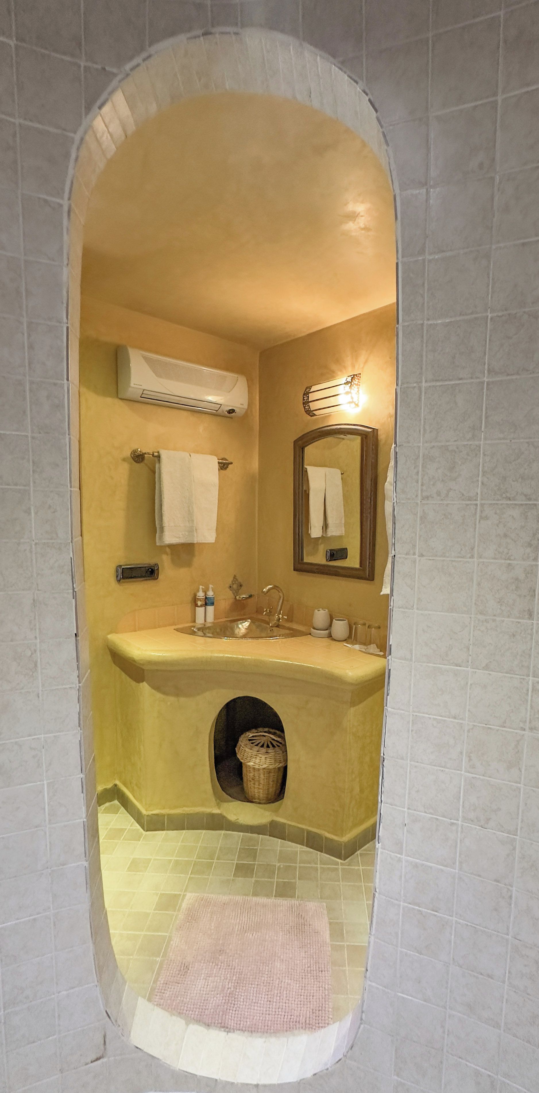 A bathroom with a yellow sink, a mirror, a towel rack, and a small basket.