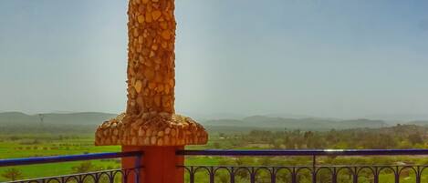 Un balcón con un pilar de piedra, una mesa con sillas y vistas a campos verdes.