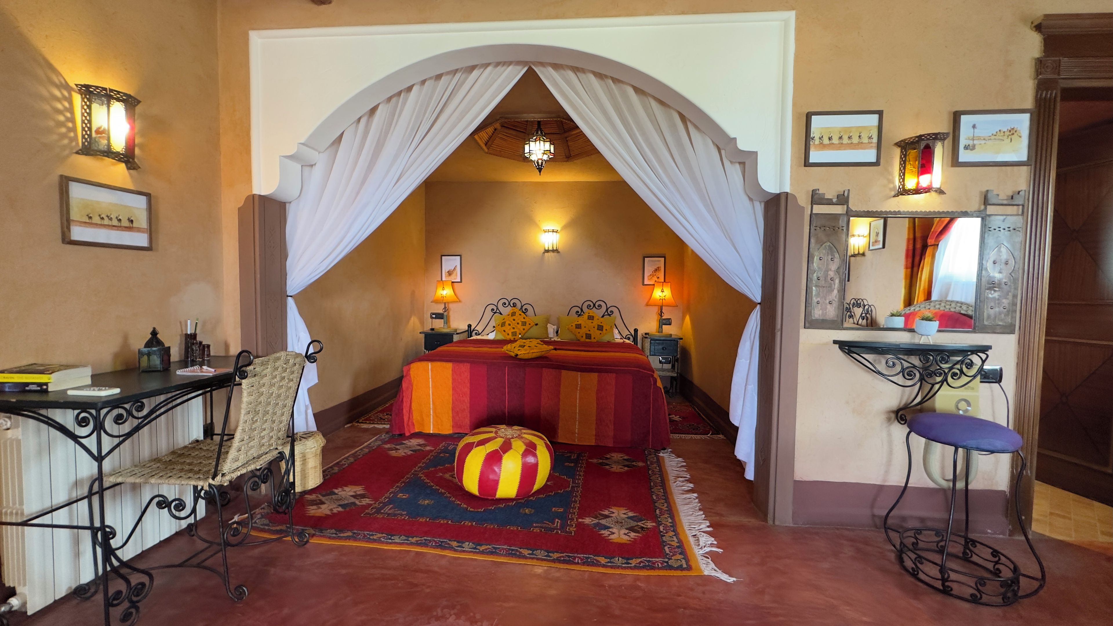 Quarto com cama, cadeira, escrivaninha e pequena mesa com luminária.