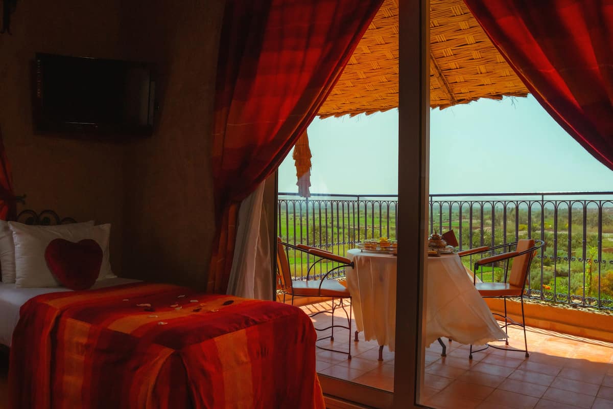 A bedroom with a bed, a TV mounted on the wall, and a balcony with a table and chairs.