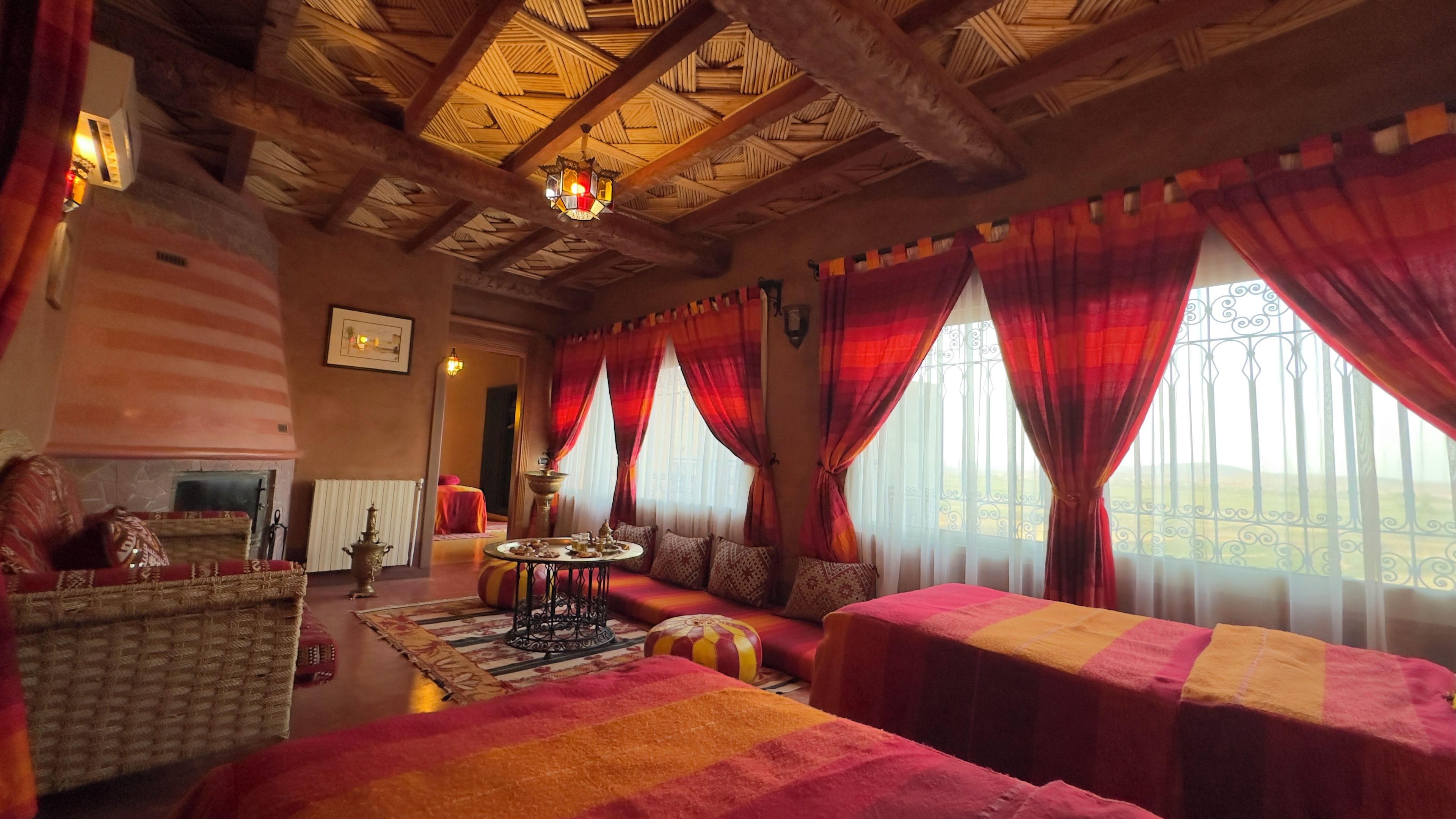 A room with a high ceiling, a fireplace, a sofa set, and a view through large windows.