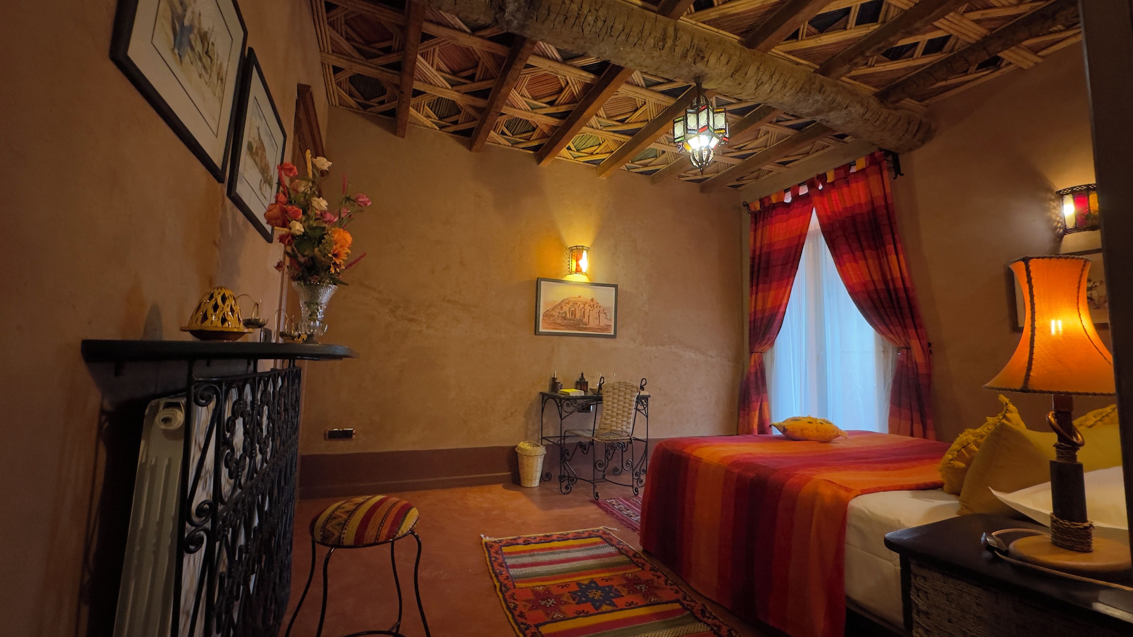 A room with a bed, a desk, a chair, a lamp, a window with curtains, and a chandelier.