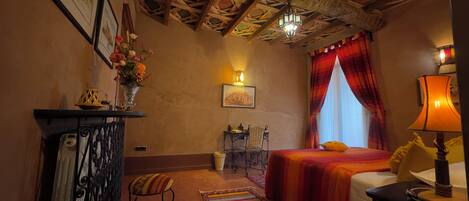A room with a bed, a desk, a chair, a lamp, a window with curtains, and a chandelier.