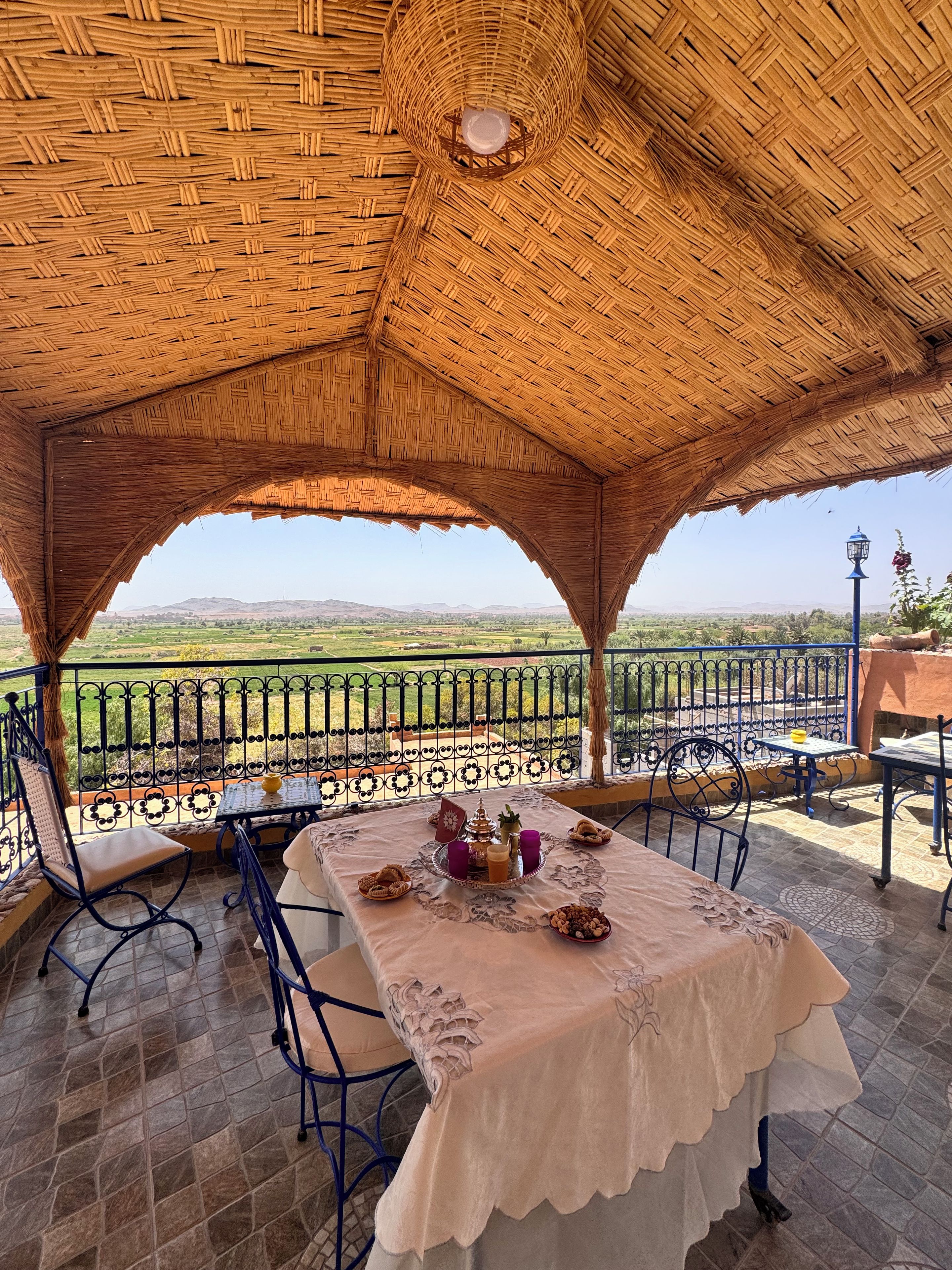 Un espace de restauration en plein air avec une table dressée pour deux personnes, une vue sur la campagne et une structure dotée d’un toit de chaume.