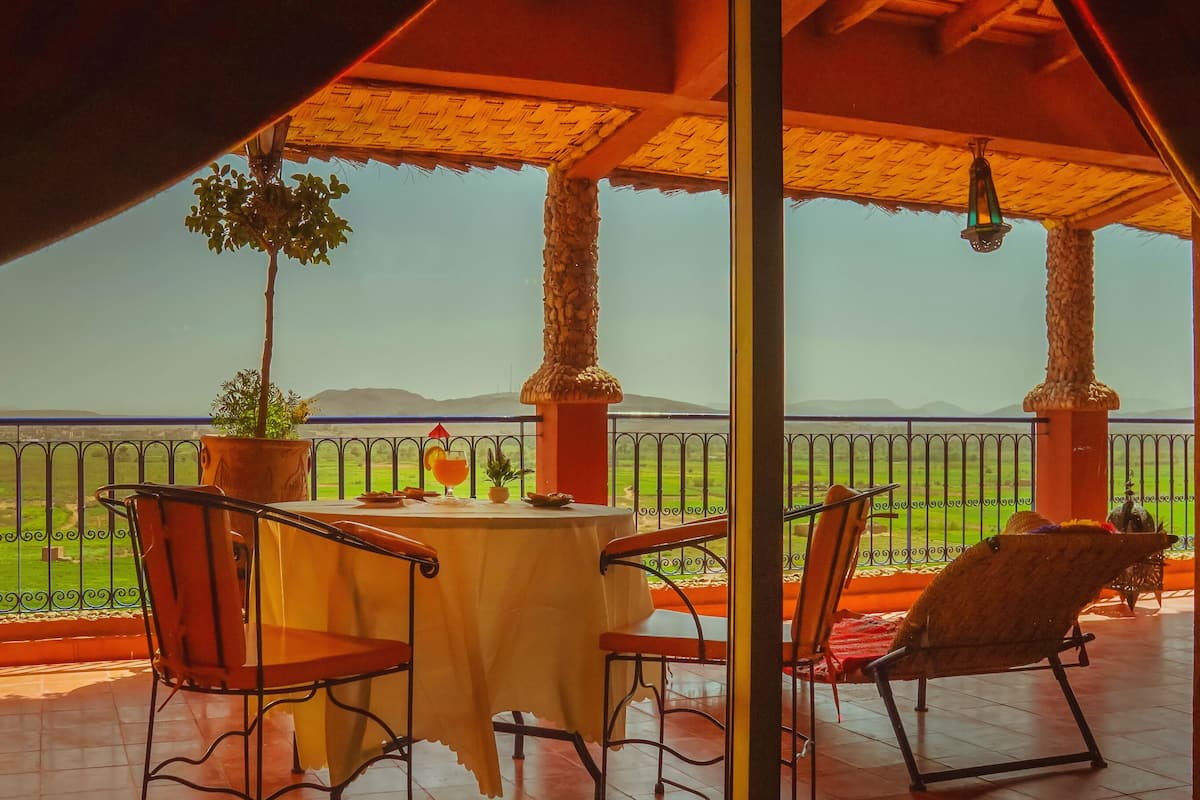 A terrace with a table and chairs, a potted plant, and a view of a green landscape.