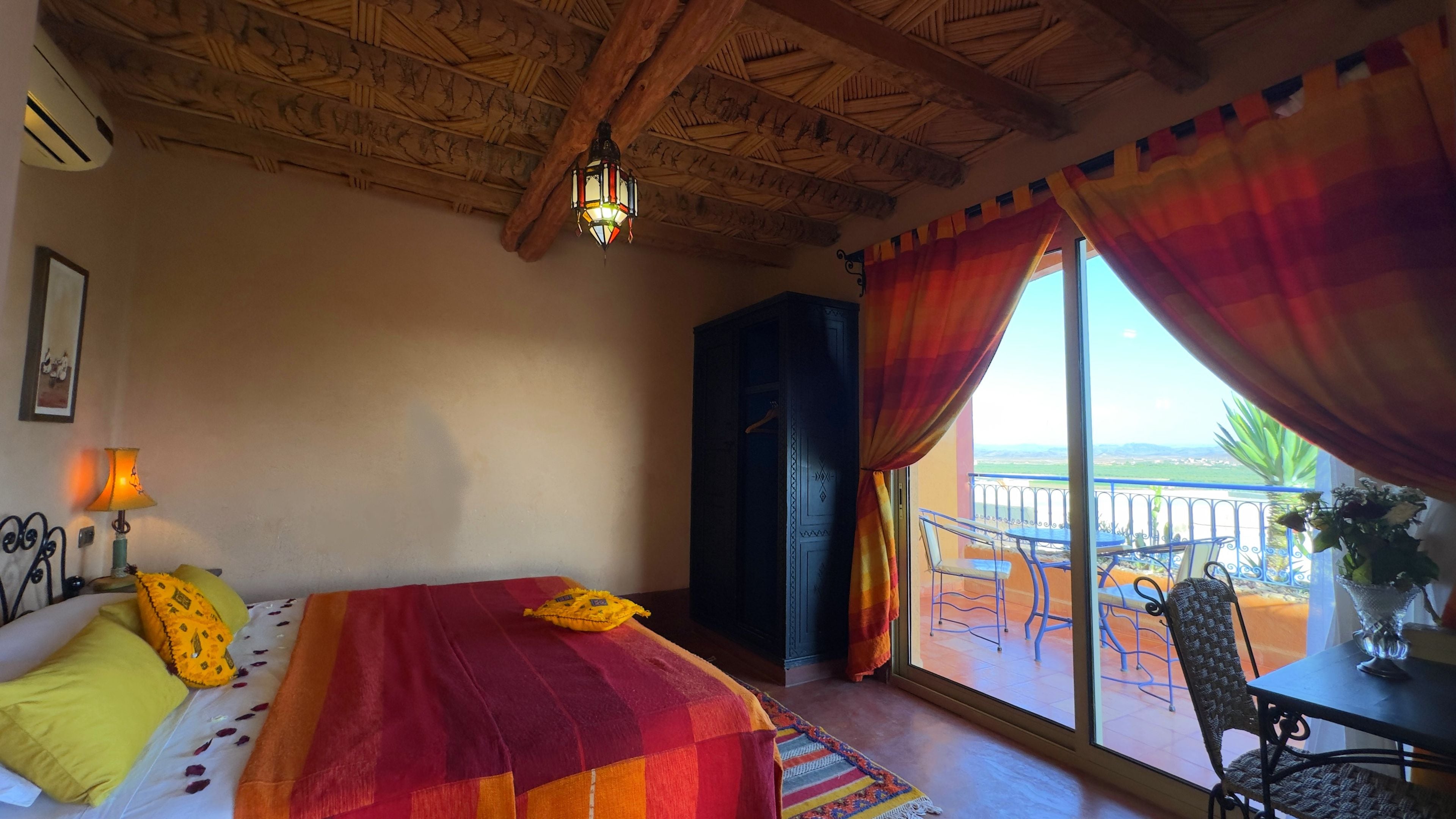 A room with a bed, a nightstand, a lamp, a window with curtains, and a view of the outside.