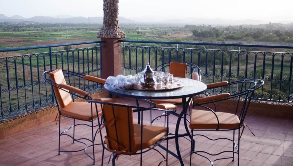 Une table ronde entourée de chaises, sur un balcon donnant sur un paysage rural.