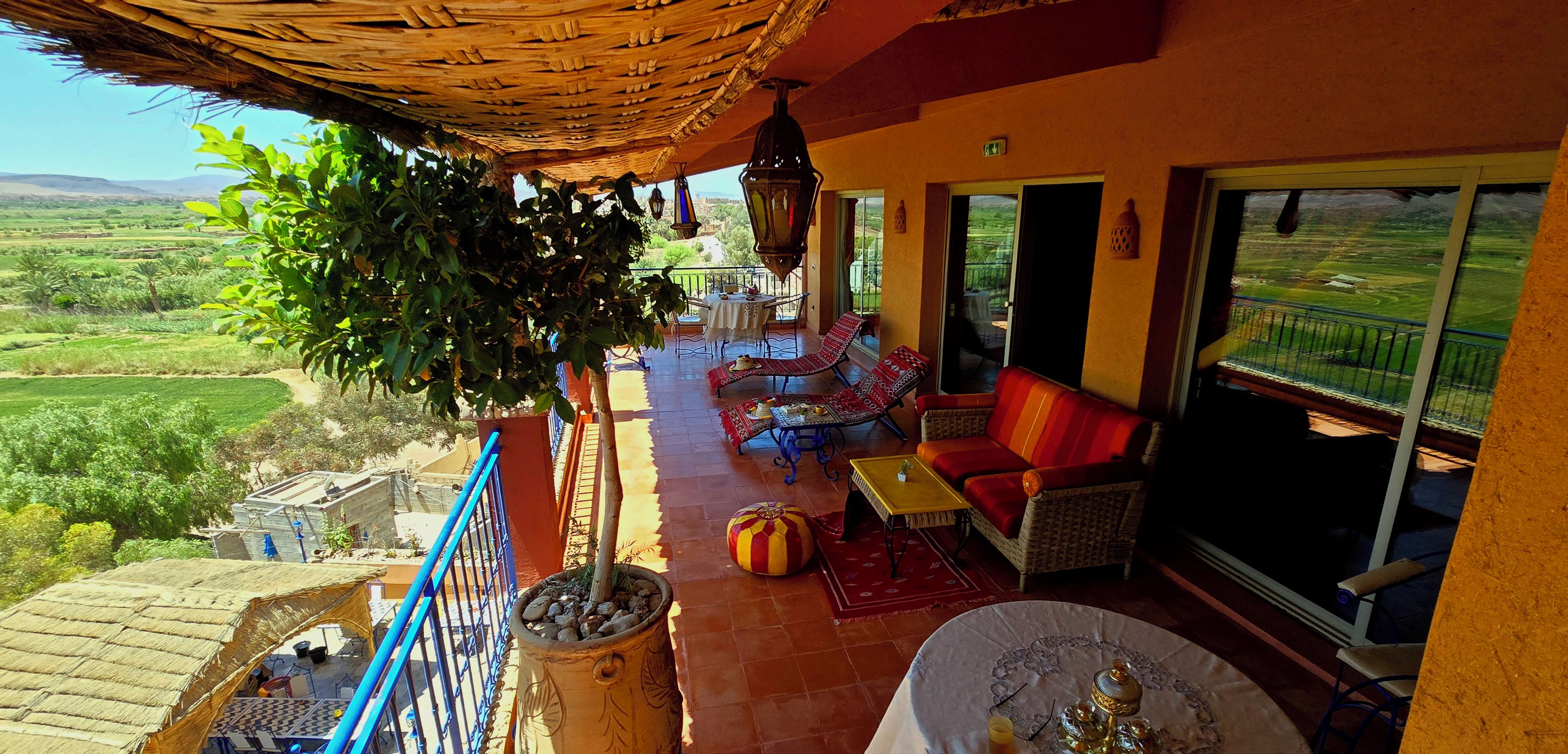 A balcony with a view of a green landscape, a seating area with a sofa and chairs, and a table with a decorative item.