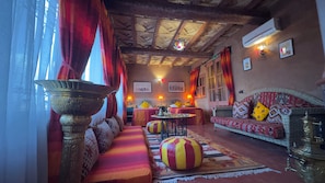 A traditional room with a wooden ceiling, a sofa set, a patterned rug, and a large brass lamp. - Dar Amoudou (Ouarzazate)