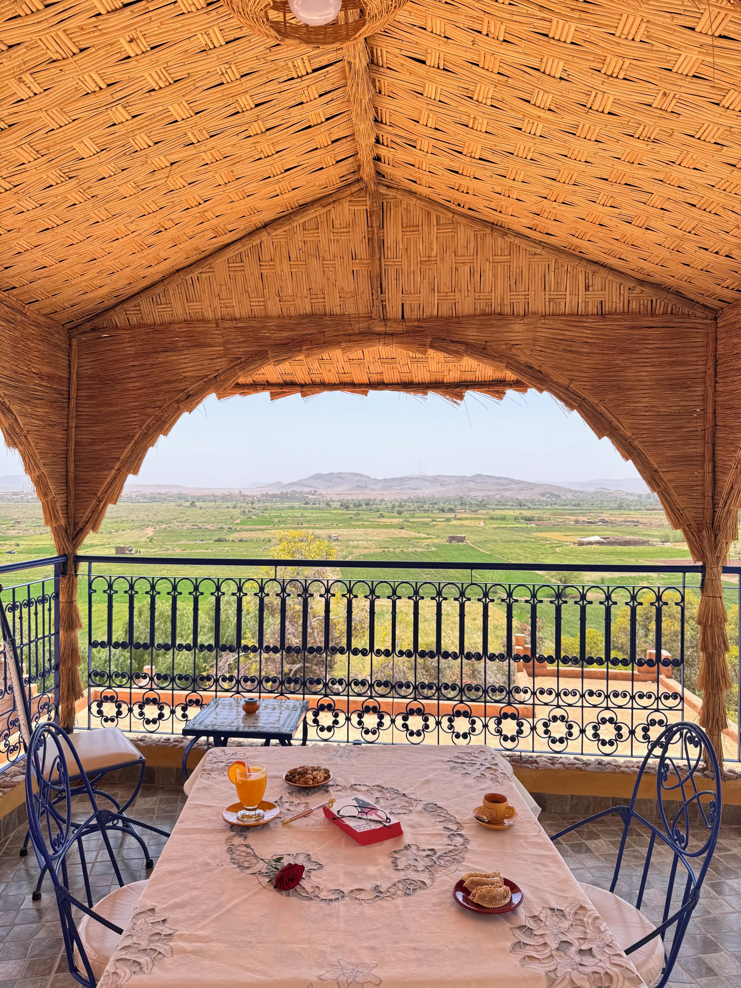 Un espacio de comedor al aire libre techado con una mesa lista para dos personas, con vista a un paisaje pintoresco.