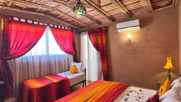 A room with a bed, two bedside tables, a ceiling fan, and an air conditioning unit.