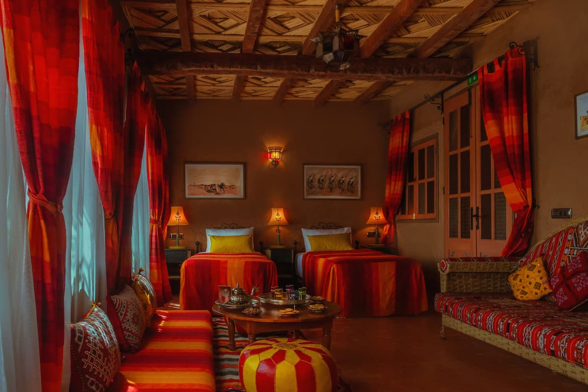 A traditional room with two beds, a sofa, a table with a tray of snacks, and a window with curtains.