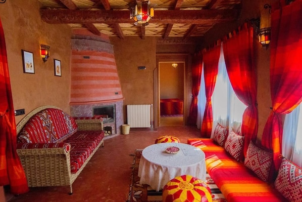 Una habitación acogedora con chimenea, un sofá, una mesa de comedor y un ventanal con cortinas rojas.