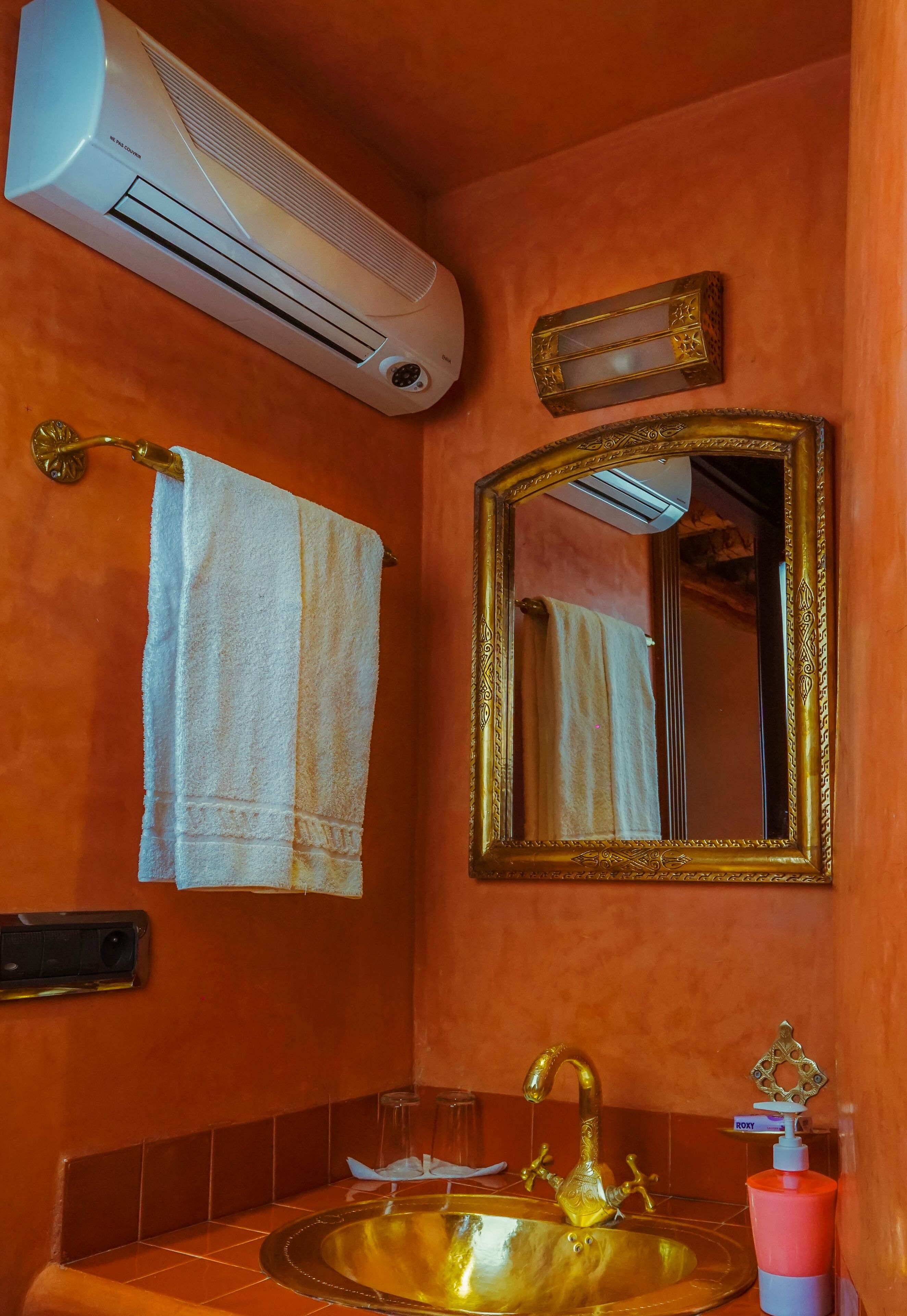 Un baño con un lavamanos dorado, una toalla blanca, un espejo con marco dorado y un equipo de aire acondicionado.