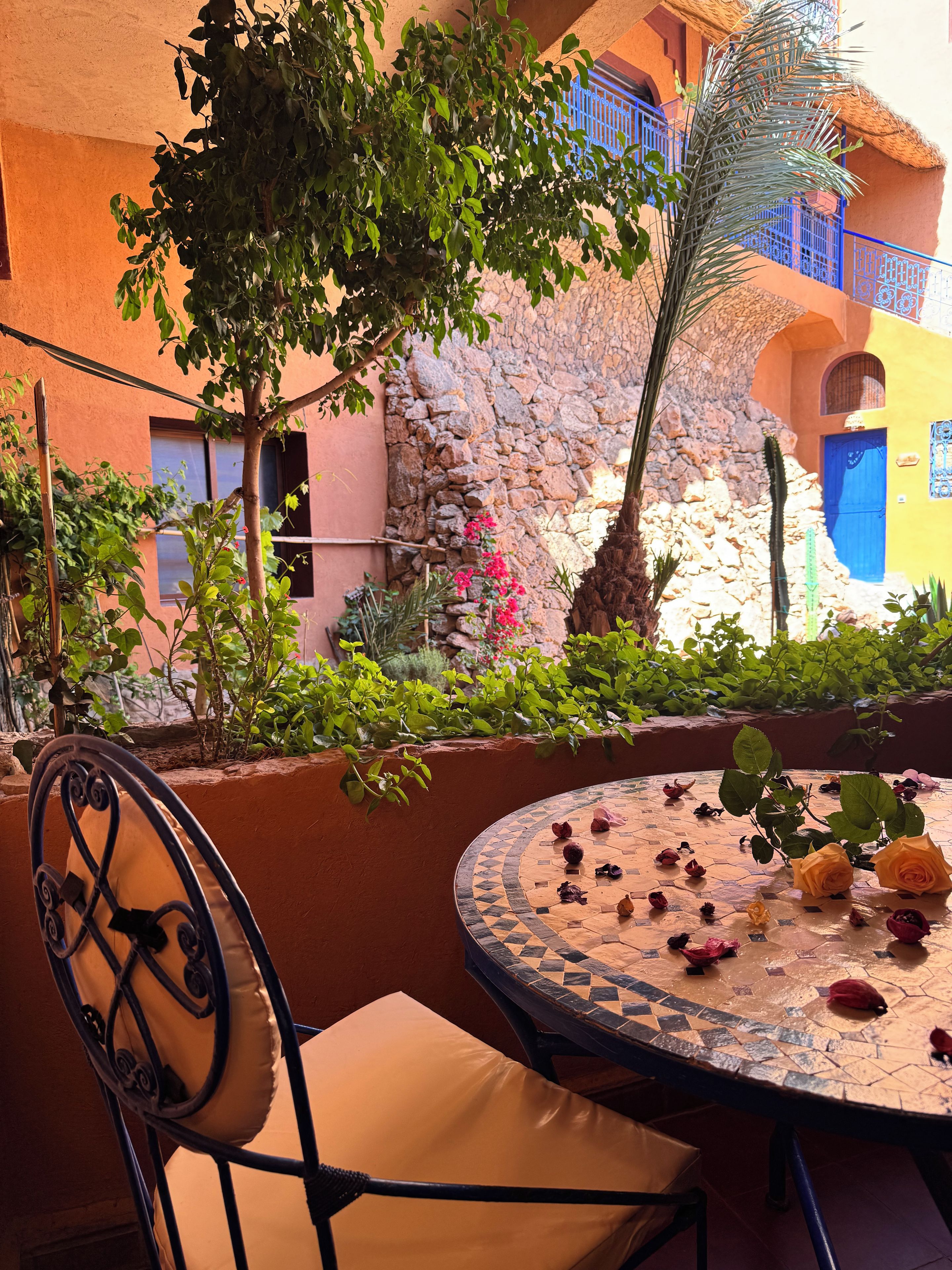 Un espace extérieur aménagé avec une table ronde et des chaises, entouré de plantes et d’un mur en pierre.