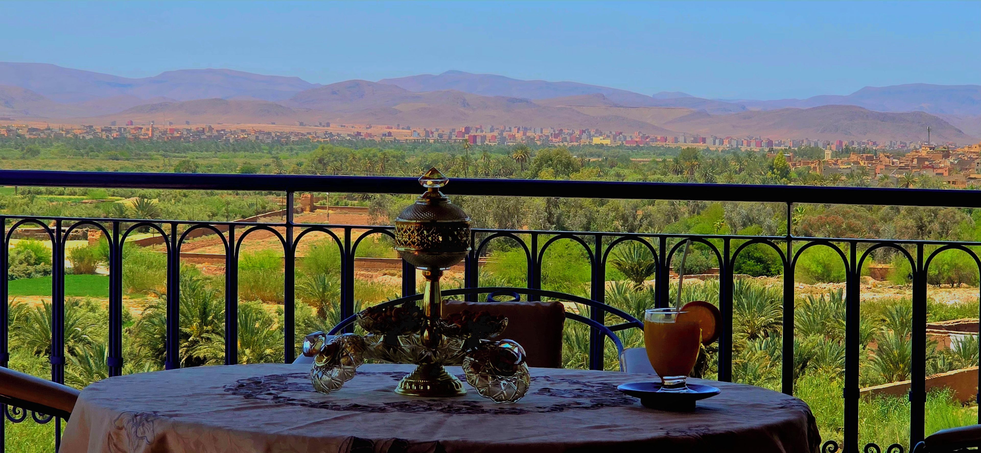 Un balcón con una mesa lista para comer, con vistas a un paisaje urbano y montañas.