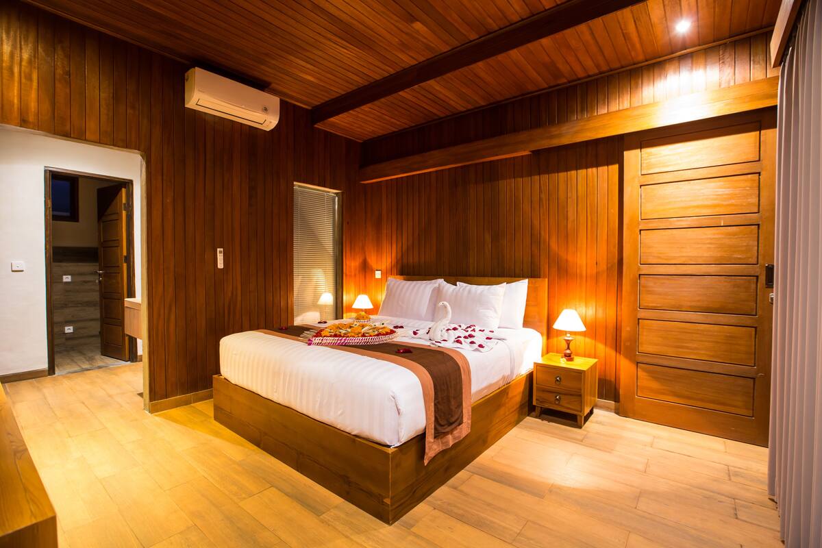 A wooden-paneled bedroom with a large bed, bedside lamps, and a wooden wardrobe.