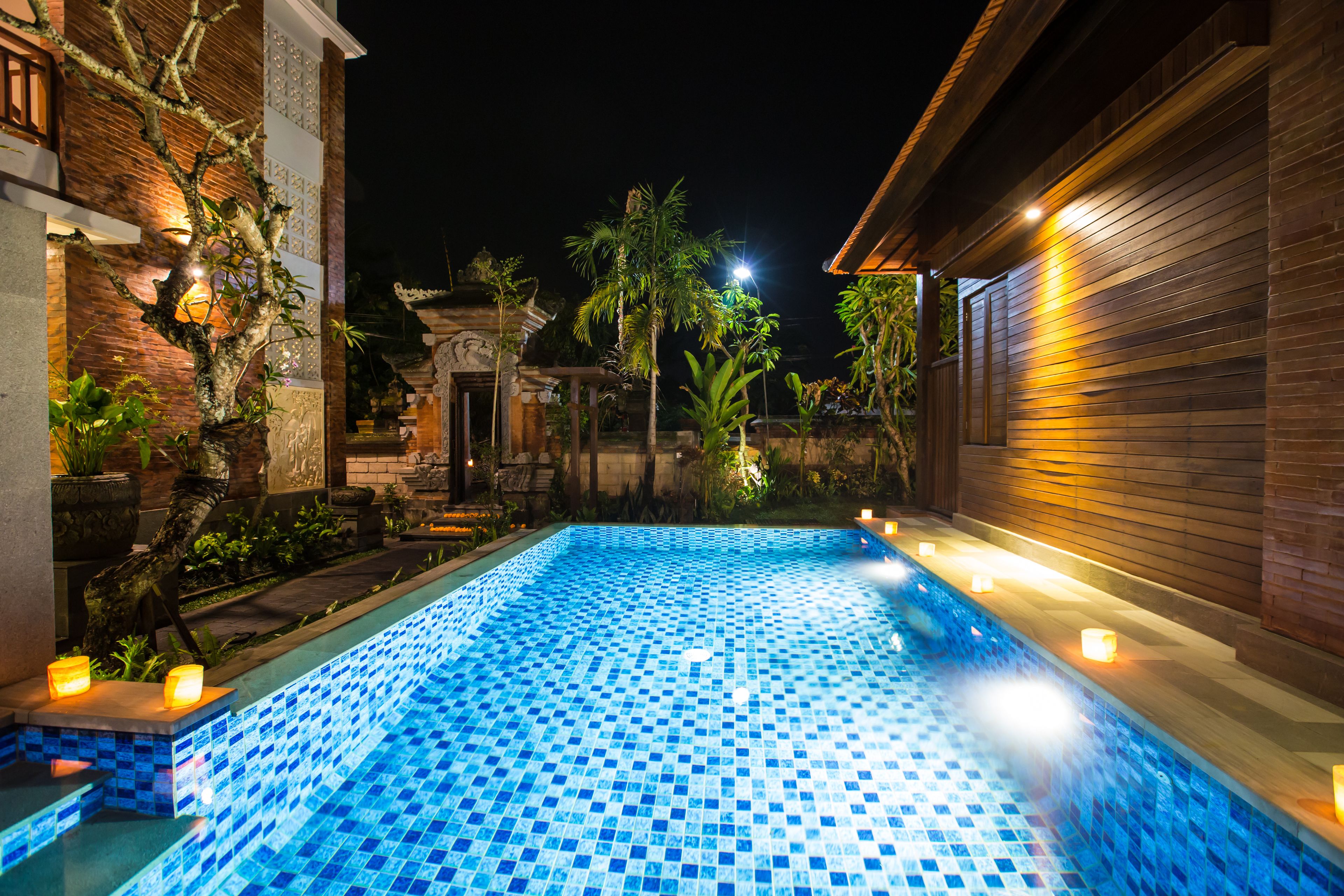 A swimming pool with tiled blue and white patterns, surrounded by a wooden deck and potted plants.
