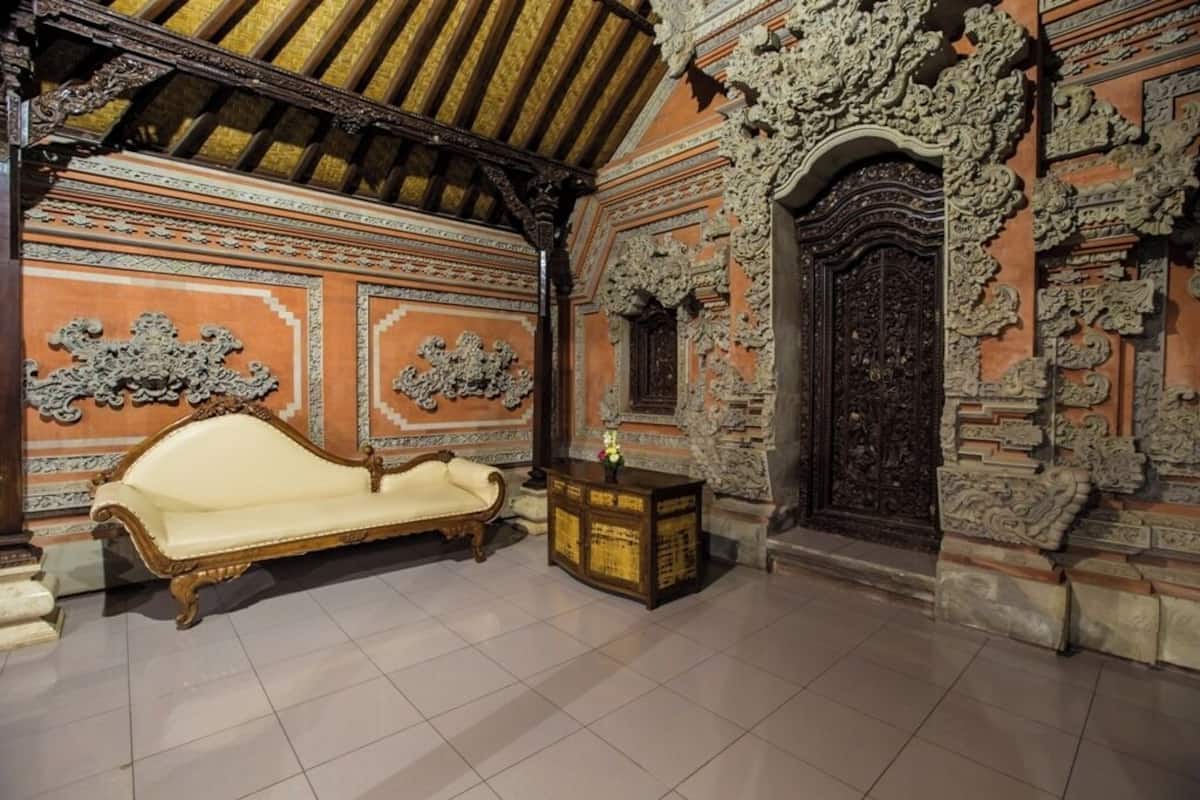 A room with a wooden ceiling, ornate wall carvings, a white sofa, and a small wooden table with a vase.