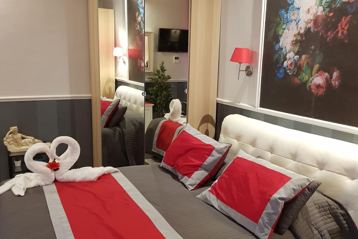 A hotel room with a large bed, a mirror, a television, and a floral painting on the wall.